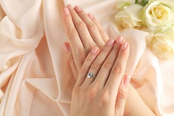 Woman wearing beautiful ring with gemstone against beige fabric, top view
