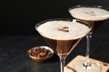 Delicious espresso martini with coffee beans in glasses on blurred black background, closeup