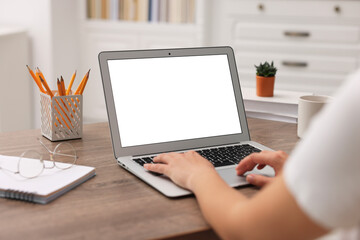 Woman working with laptop at wooden table in office, closeup. Mockup for design