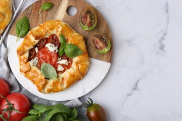 Tasty galette with tomato, basil and cheese on white marble table, flat lay. Space for text