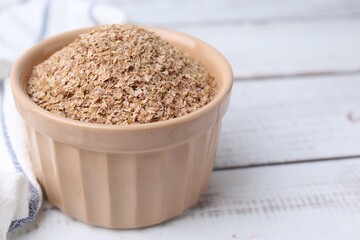 Buckwheat bran in bowl on white wooden table, closeup. Space for text
