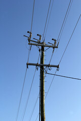 Wooden power electricity pole with multiple wires and insulators against a clear blue sky