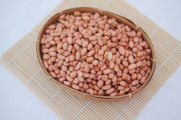 Peanuts in a basket on a bamboo mat, top view.