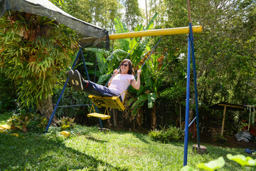 Portrait of a happy girl with Down syndrome on a swing. Happy little girl in the yard swinging on the seesaw. Summer outdoor activities for . Trisomy 21.