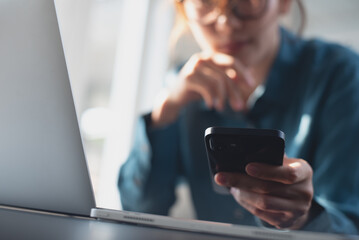 Close up, young smart business woman using mobile phone, looking at the screen during working on laptop computer at modern office. Student studying online class, using smartphone and laptop computer