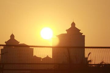 The stunning silhouettes of the buildings are framed by the bright orange of the sunset, creating a...