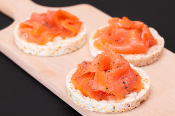 Tasty Rice Cake Sandwiches with Fresh Salmon Slices on Wooden Cutting Board. Easy Breakfast and Diet Food. Crispbread with Red Fish. Healthy Dietary Snack