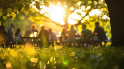 Blurry silhouettes of picnickers at a park gathering with the sun casting a warm glow through the trees.