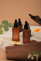 Frosted and Amber Glass Dropper Bottles with Floral and Fabric Decor on Beige Background