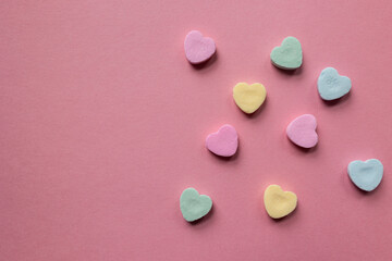 flat lay of scattered pastel colored candy hearts in pink, green, and yellow against a pink background with copy space available; valentines day themed