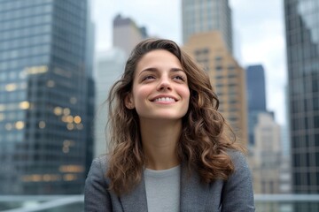 Fototapeta premium A smiling woman with curly hair poses confidently against a backdrop of urban skyscrapers.