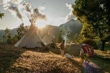 Native community with people in a landscape with teepee and temazcal in a sunrise with the sun rising over the mountains. 