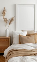 Cozy bedroom setup with neutral tones, featuring pillows, a soft blanket, and decorative vase with dried plants on a bedside table against a minimalistic wall.