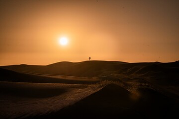 Silhouette scene of a man standing on a dune against red dusk sky watching sunset