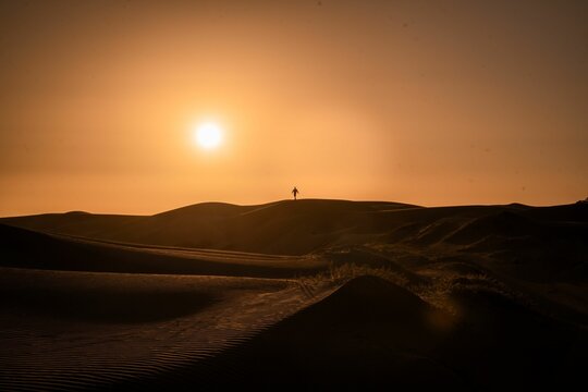 Silhouette scene of a man standing on a dune against red dusk sky watching sunset