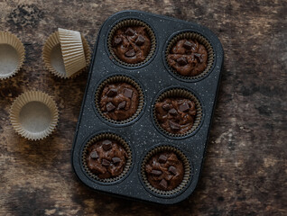 Making chocolate muffins with chocolate pieces on a wooden background, top view
