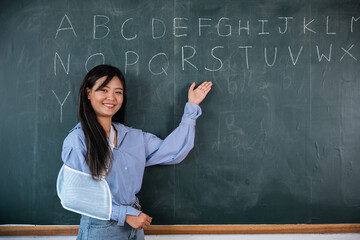 A woman is teaching class in a school. She is pointing to the alphabet on the blackboard. Arm...