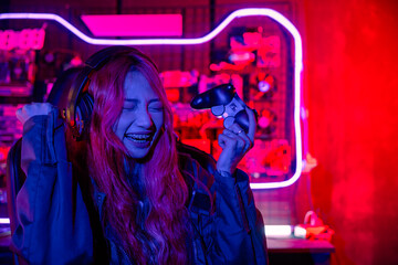 Winning. Happy Gamer using joystick controller for virtual tournament plays online video game with computer she raises hands to wins celebrating, Asian woman wearing gaming headphones feeling excited