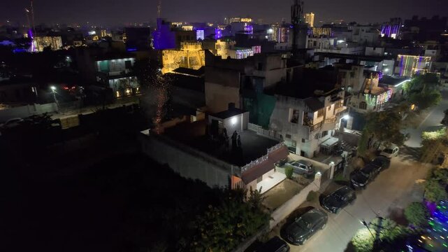 Aerial drone flying backward between small houses with group of people bursting fireworks rockets, sky shots from roof of house during the hindu festival of diwali