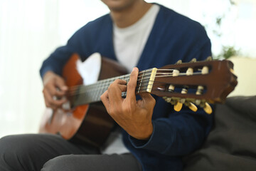 Young asian man relaxing and playing acoustic guitar in living room