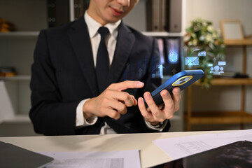 Businessman in black suit using smartphone with virtual data icons for connectivity and business growth