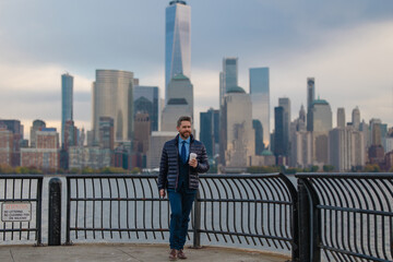 Fototapeta premium Handsome businessman in NYC. Outdoor business. Serious businessman standing against skyscraper in New York, at Manhattan. Professional employee waiting for business partners outdoors.