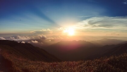 Stunning panoramic view of a mountain range at sunset with golden rays of sunlight illuminating the clouds and peaks.
