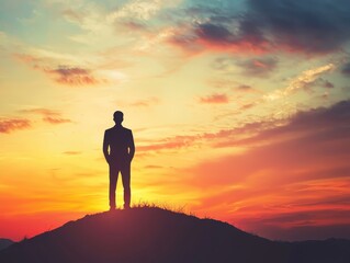 Obraz premium A silhouette of a person standing atop a hill, gazing at a vibrant sunset with colorful clouds, evoking feelings of solitude and reflection.
