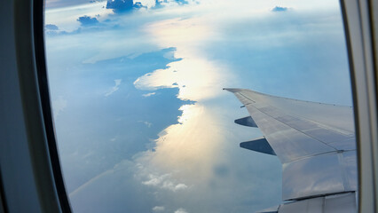 Fototapeta premium View from an airplane window of an airline wing slices through dense, dramatic clouds, glinting in soft sunlight, evoking a sense of mystery, wonder, and endless possibilities beyond the horizon.
