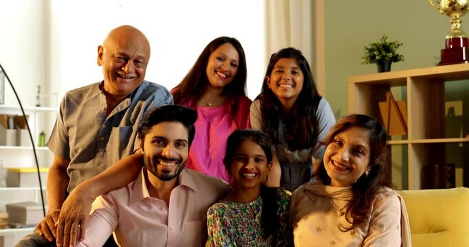 Closeup of Indian Asian multigenerational family of six sitting together on a sofa in a luxurious home, sharing happy moments and bonding across generations