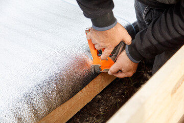 A man is using a staple gun to attach a piece of insulation to a wooden board