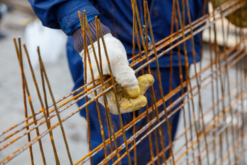 A man wearing a blue jacket and gloves is holding a piece of wire