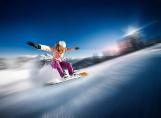 A snowboarder, dressed in a pink and white outfit, glides down a snowy mountain slope with arms outstretched, against a backdrop of a clear blue sky with a sun shining brightly.
