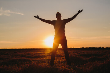 Fototapeta premium Man with Arms Outstretched in Field at Sunset