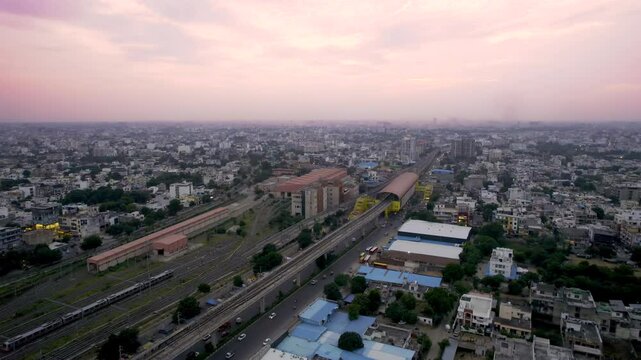 aerial drone shot flying sideways over elevated metro monorail train tracks with station and a parking yard for the trains surrounded by house, buildings offices in India