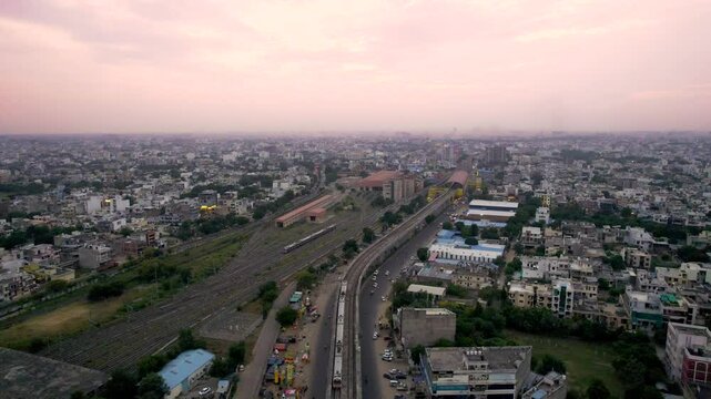 aerial drone shot following metro train on elevated track going to station as it passes between buildings, houses, homes in the densely populated city of jaipur, lucknow, hyderabad, cochin