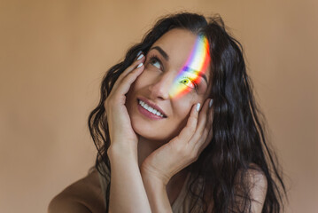 Portrait of brunette girl with rainbow on her face. Multicolored light in studio. LGBT symbol...