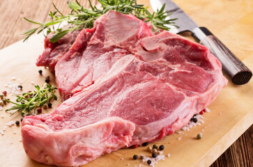 Raw dry aged chianina porterhouse beef steak with pepper and rosemary offered as close-up on a wooden design board