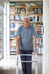 Elderly man, walking frame and portrait in library at nursing home with mobility, balance and recovery in retirement. Senior person with disability, rehabilitation and healing with injury in Spain