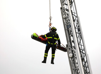 Brave firefighter hanging from ladder with stretcher carrying injured person in rescue operation