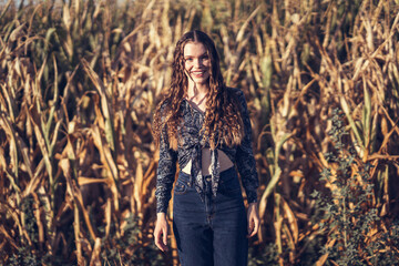 A young woman in a cornfield shows off her curly hair and stylish outfit with confidence