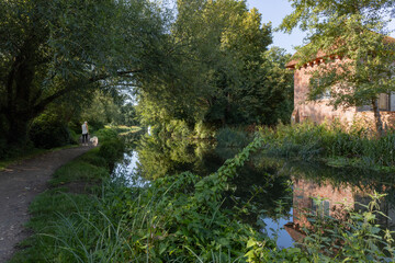 Woman walks dog alongside historic red brick building on River Wey Navigations on a stretch of the canal near Ripley in Surrey, and close to Woking