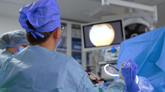 Rear view of a working surgeon applying tool devices. Doctor operated traumatized knee.