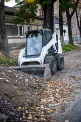 The modern skid steer small excavator working with soil on construction site. Autumn