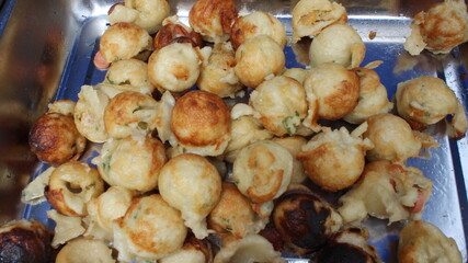 Street vendor cooking takoyaki on a hot griddle.