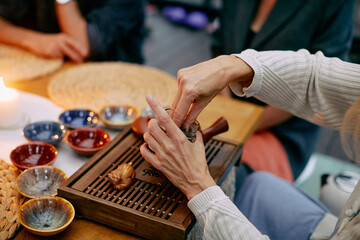 Hands performing a tea ritual on a bamboo tray surrounded by teacups, emphasizing the serene and cultural elegance of the traditional ceremony