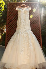Boho lace wedding dress hanging on a wooden rack with greenery in the background