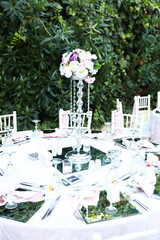 A romantic and elegant outdoor wedding reception with round tables, white chairs, and a floral...
