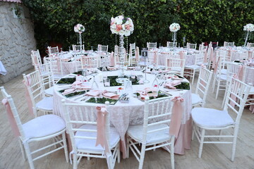 A romantic and elegant outdoor wedding reception with round tables, white chairs, and a floral...