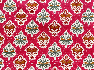 Fototapeta premium A soft pink cotton fabric adorned with green and maroon geometric floral buttas, intricately block-printed in a symmetrical checkered pattern.